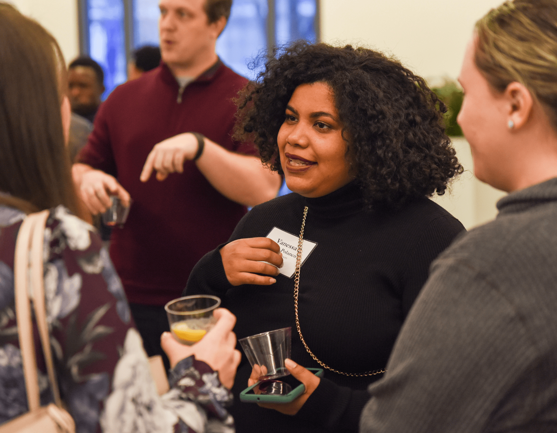 Image of a woman chatting with others and enjoying a drink at a networking reception