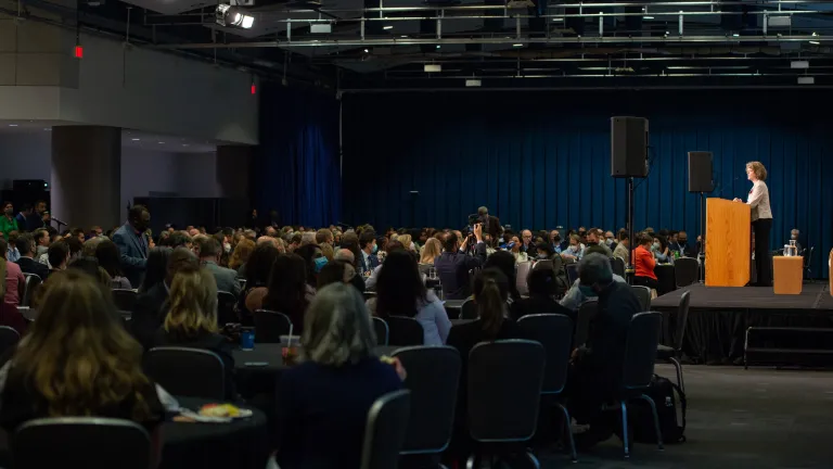 Wide shot with audience on left and stage with speaker in focus on right