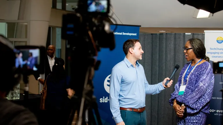 Behind the scenes shot of two people in front of a camera, person on right is being interviewed